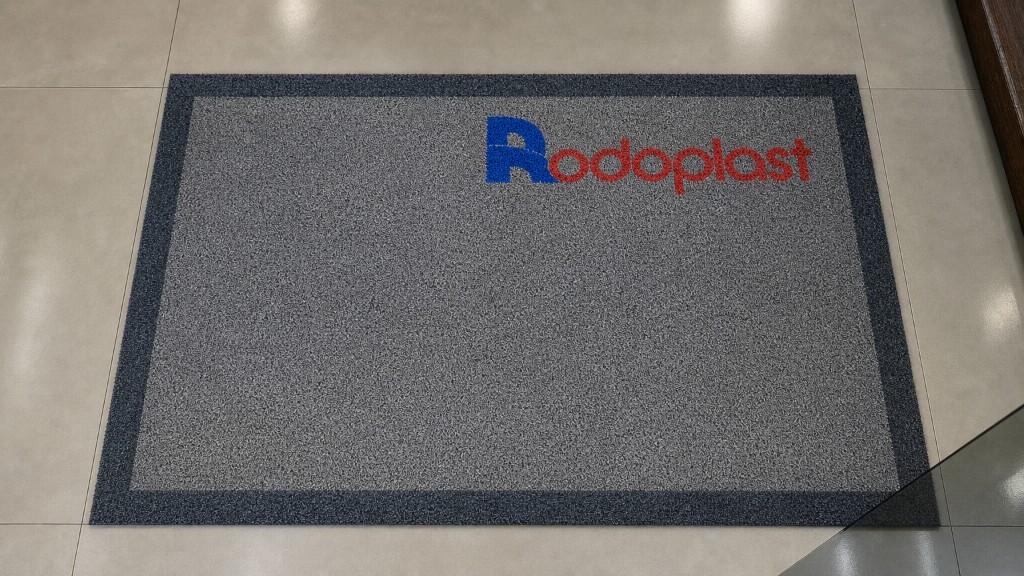 Capacho personalizado da Rodoplast com o nome da marca em destaque, instalado na entrada sobre piso premium, ideal para empresas e estabelecimentos comerciais.