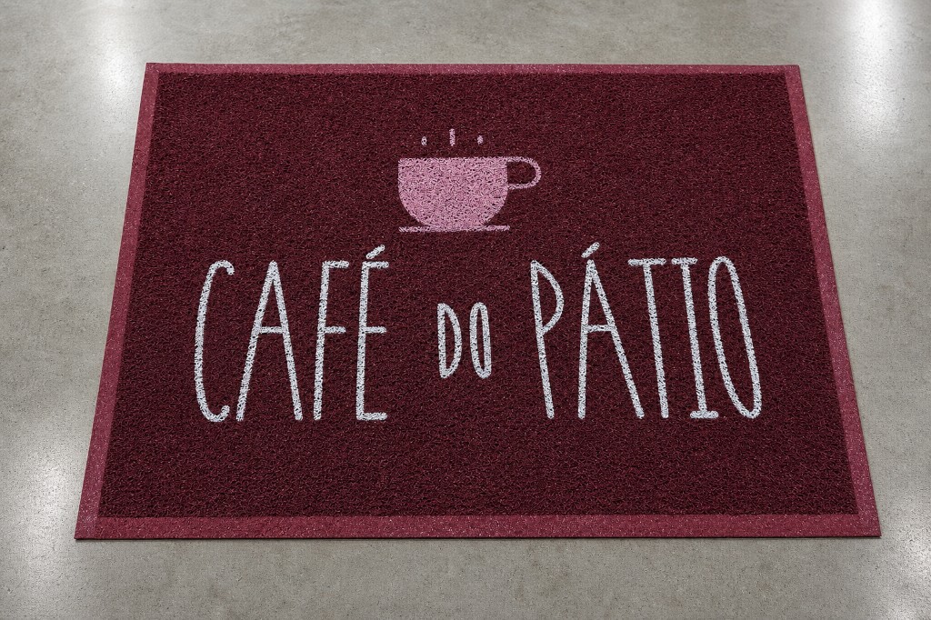 Capacho personalizado do Café do Pátio em bordô com o nome em branco e o ícone de xícara de café, instalado na entrada sobre piso premium, em Vacaria/RS, ideal para cafeterias e estabelecimentos comerciais.