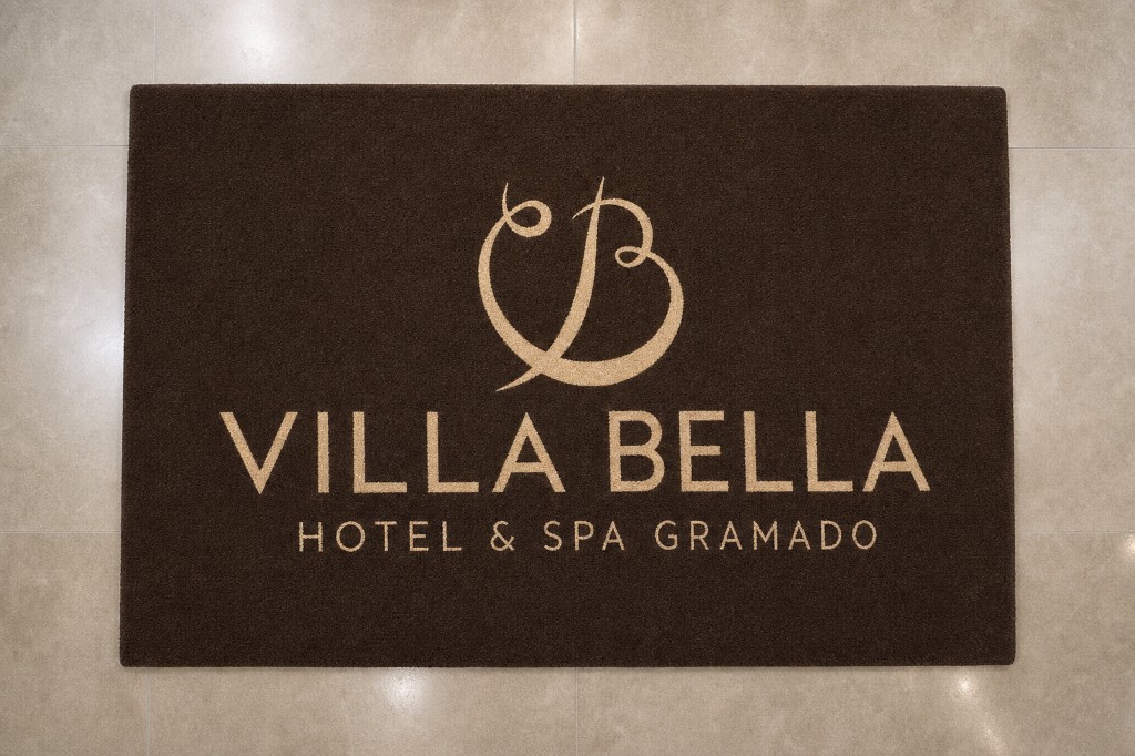 Capacho personalizado do Villa Bella Hotel & Spa Gramado em marrom com o nome e logo em bege, centralizados, instalado na entrada sobre piso premium, ideal para hotéis, spas e estabelecimentos de hospitalidade.