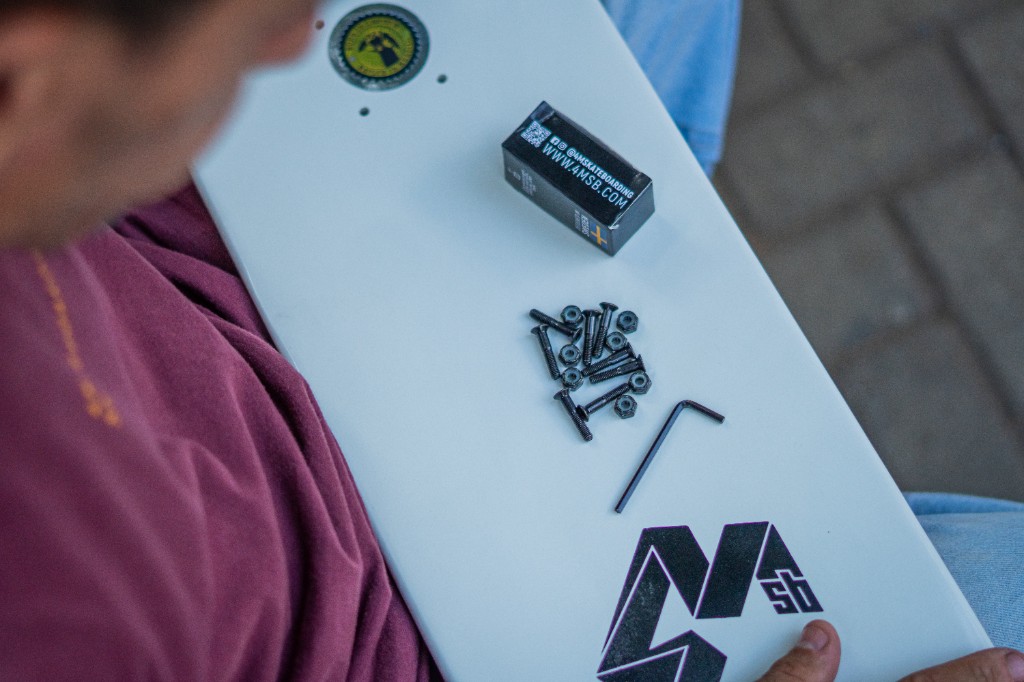 Detalhe de shape de skate 4Msb com tecnologia TIPtech, parafusos e chave de montagem, refor&ccedil;ando durabilidade e manuten&ccedil;&atilde;o inteligente