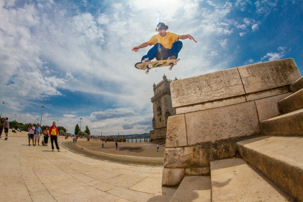 Skatista executando um Ollie com alta amplitude em frente à Torre de Belém. O uso de um shape 4Msb com tecnologia TIPtech garante que o pop permaneça nítido e seco, essencial para vencer obstáculos urbanos sem que a madeira perca a pressão.