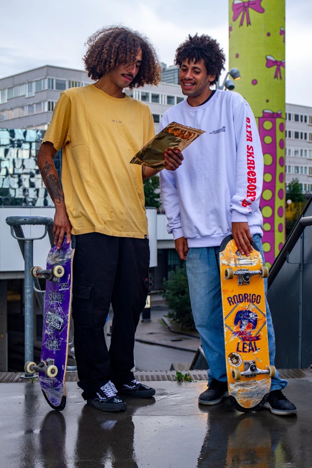 Dois skatistas conversando em um pico de rua, acompanhados de seus shapes de skate da 4Msb, incluindo o pro model amarelo Rodrigo Leal.