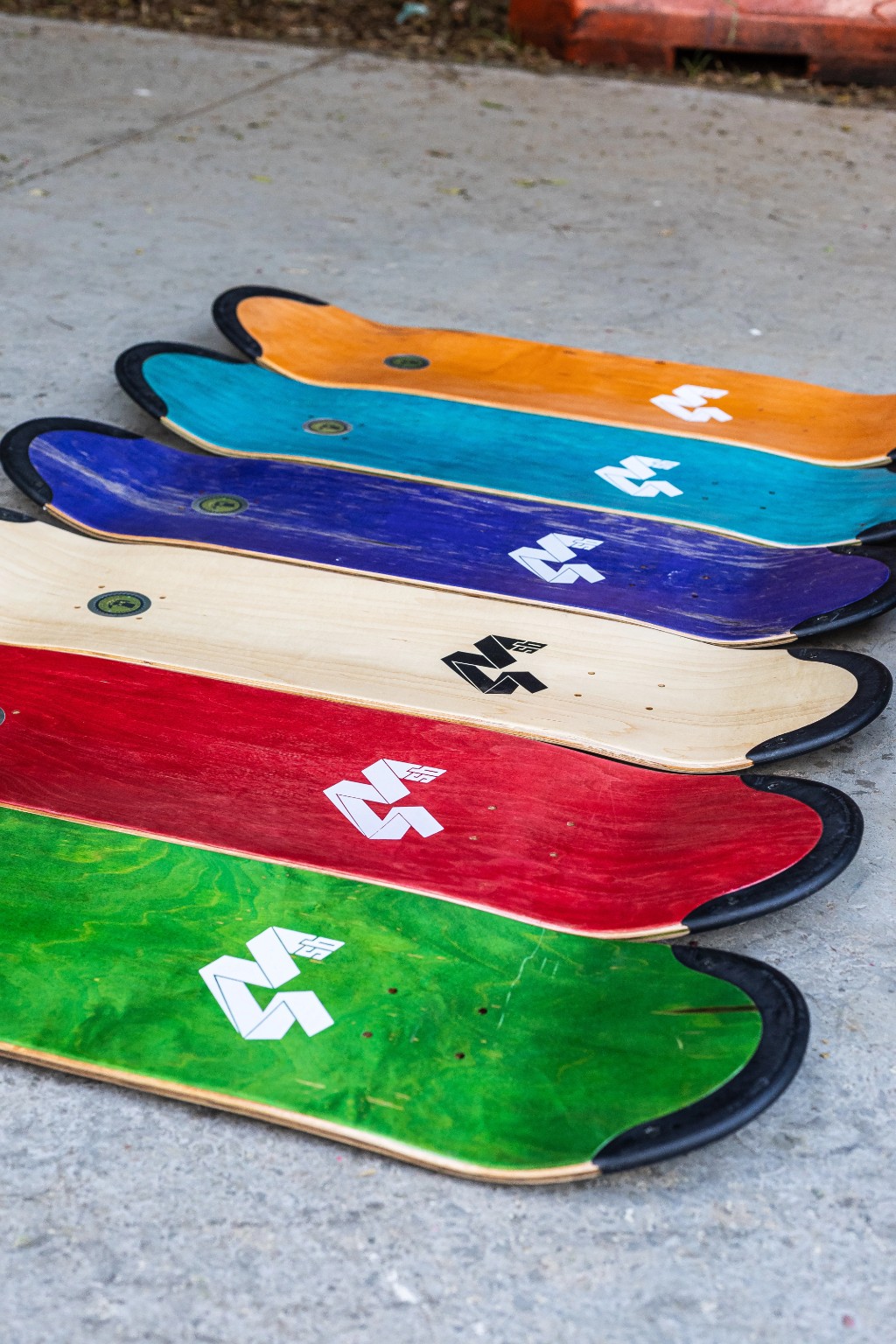 Linha colorida de shape skates de maple da 4Msb alinhados no chão, destacando a inserção preta da tecnologia TIPtech nas extremidades para garantir um pop duradouro.