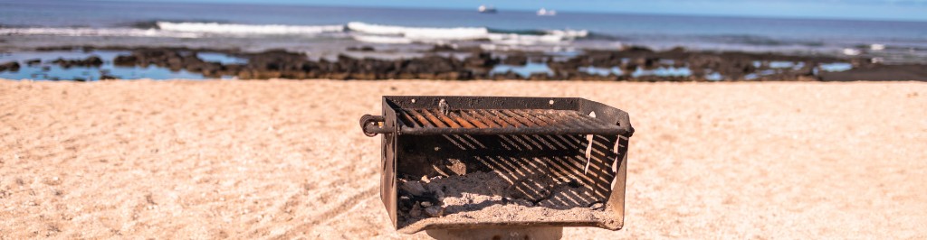 Parrilla port&aacute;til Grill West en la playa con fuego encendido