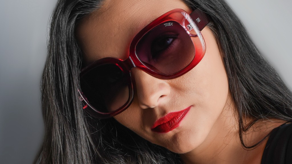 Close-up dram&aacute;tico de mulher com &oacute;culos de sol geom&eacute;trico TRIIIX, luz e sombra em ambiente urbano sofisticado.