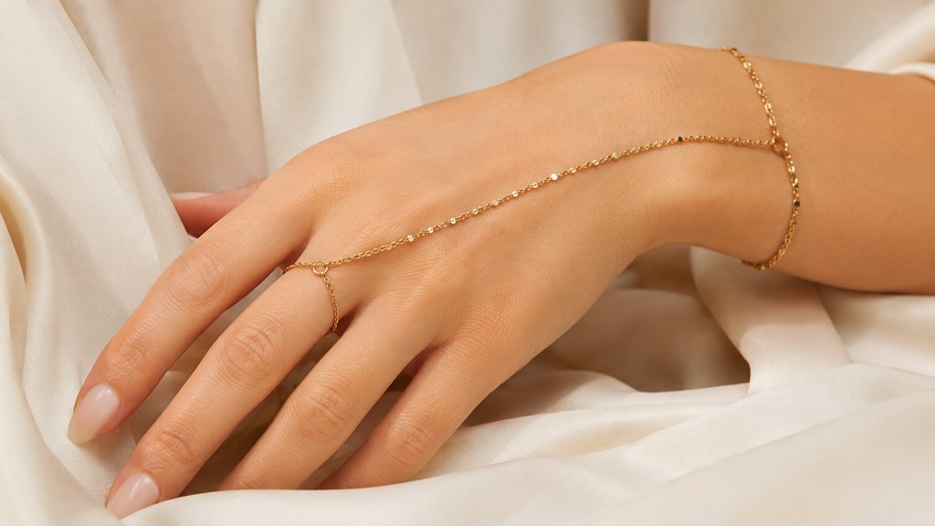 M&atilde;o elegante com hand chain dourada sobre tecido creme