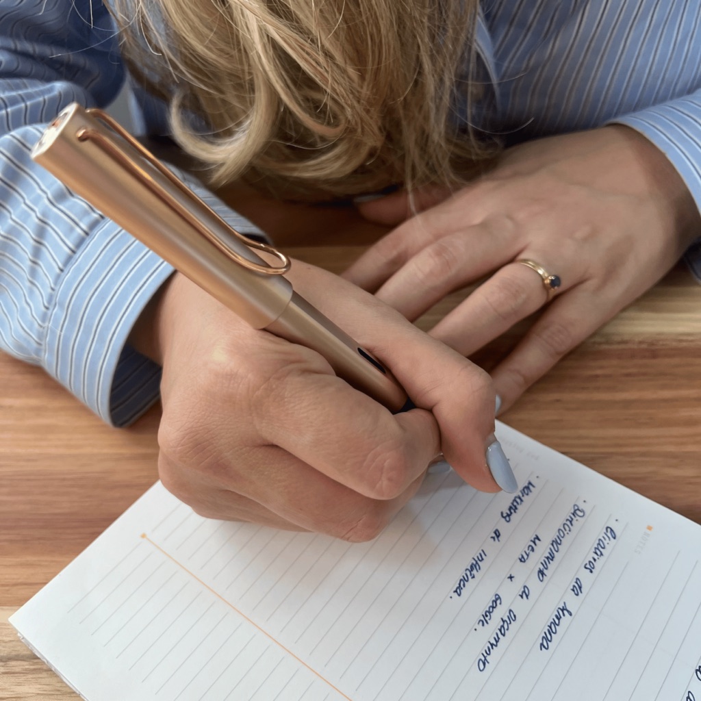 Mão escrevendo com uma LAMY AL-Star dourada em um caderno