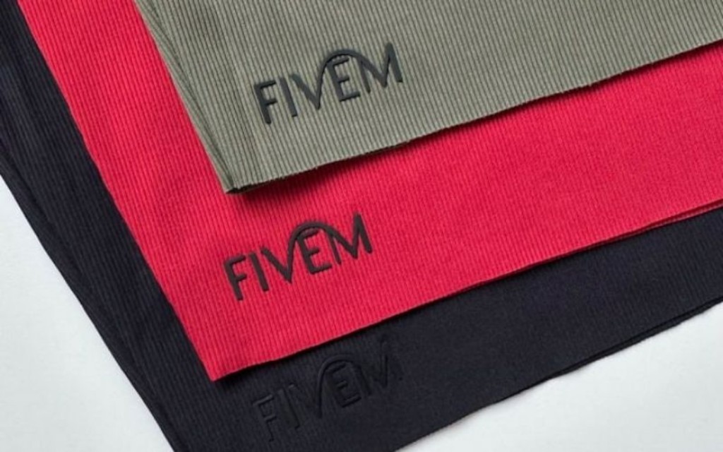  Imagem com zoom focado na etiqueta termocolante das roupas da Fivem, nas cores verde, vermelho e preto. 