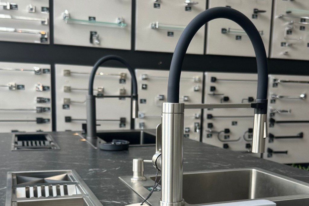 Imagem da loja na Av. Colombo. Duas torneiras modelo Dubai instaladas em cubas do mostruário. Atrás, estão instalados kits de acessórios para banheiro como papeleiras, porta toalhas e cabides.