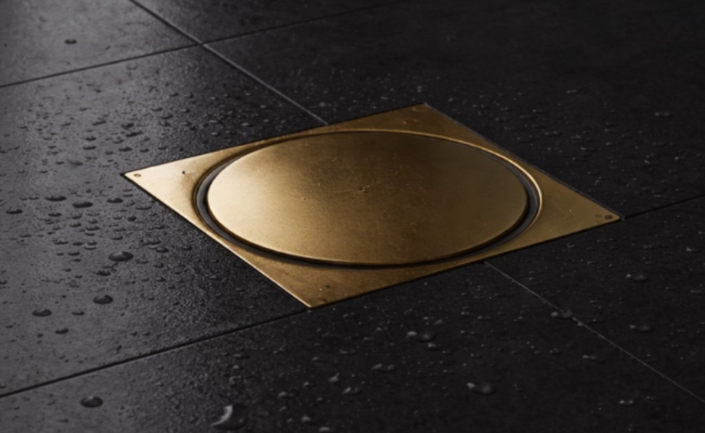 Imagem de um ralo dourado fosco instalado no chão de um box de banheiro