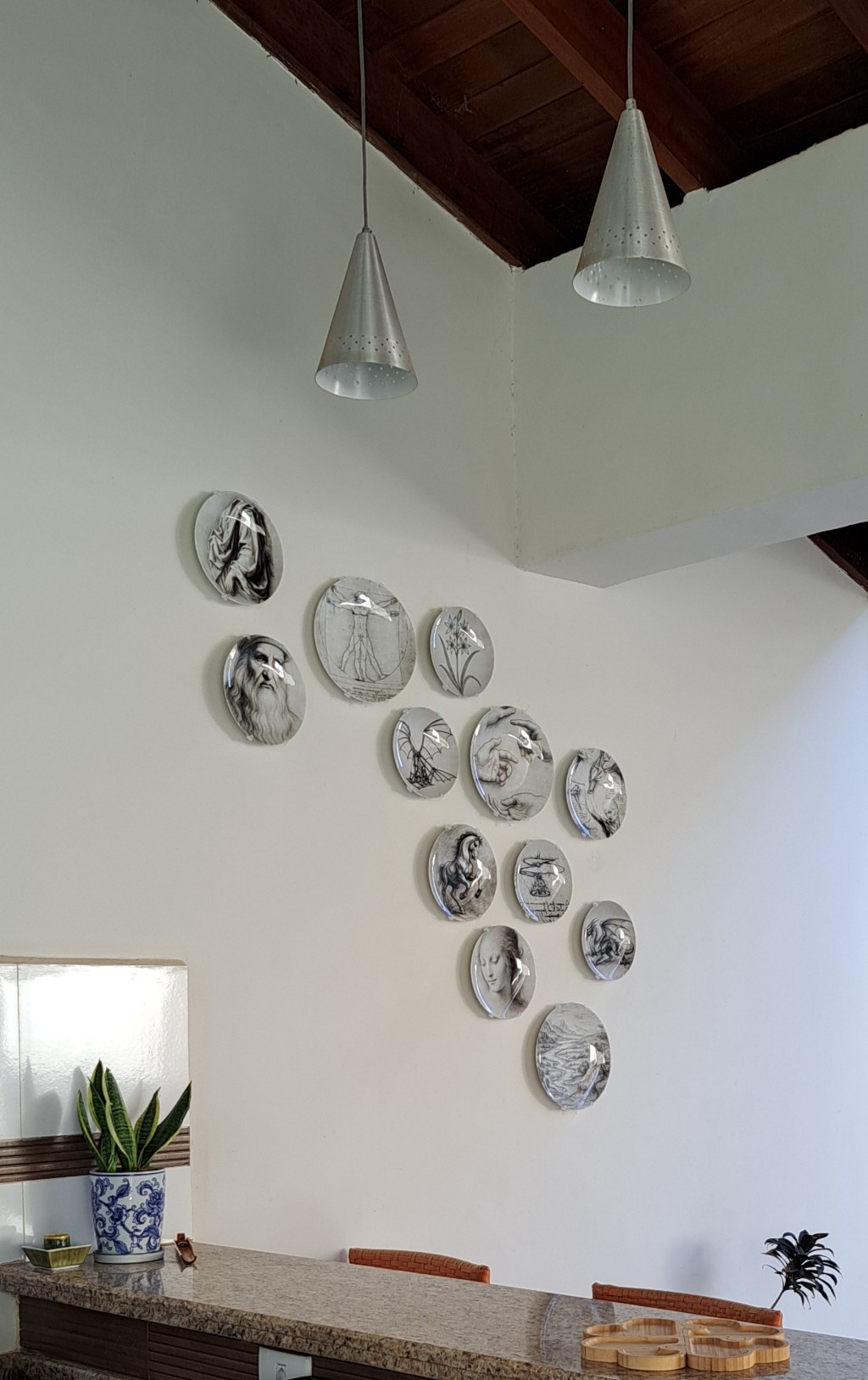 Arranjo assim&eacute;trico de pratos decorativos com estampas das obras de Leonardo da Vinci em parede de destaque na sala de jantar.