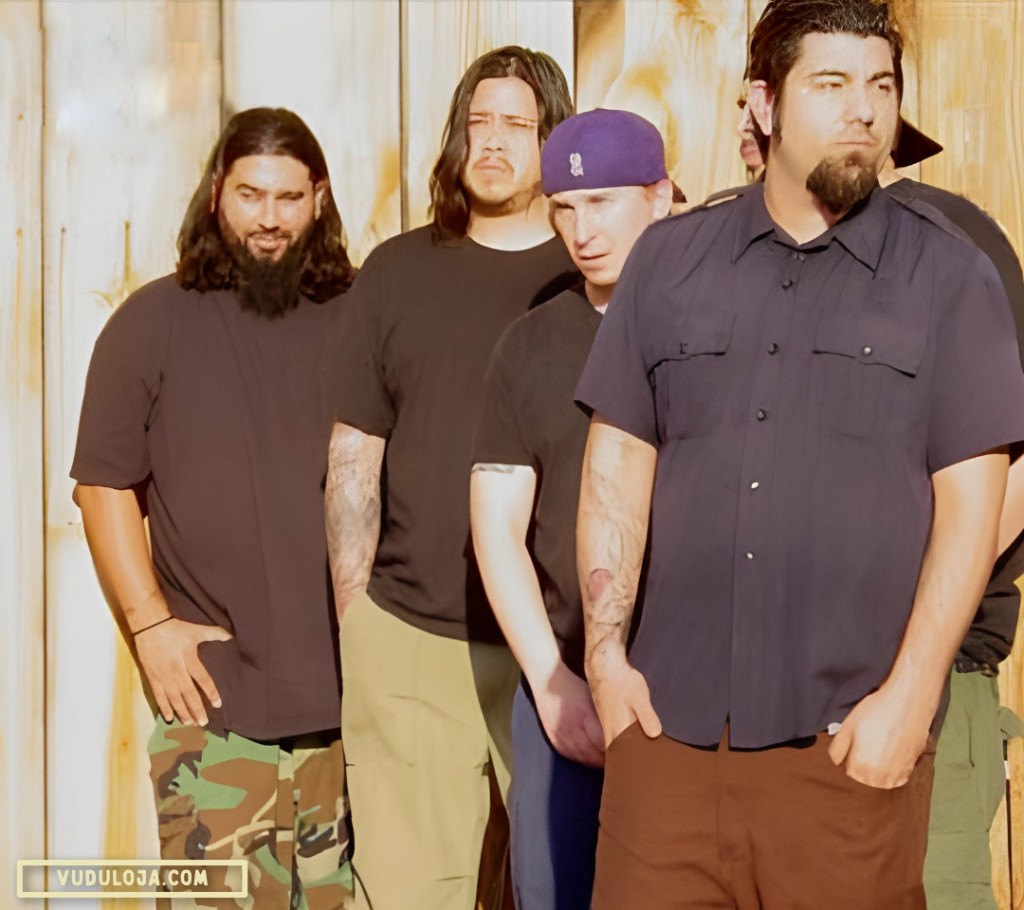 Foto colorida dos integrantes da banda Deftones, o homem em primeiro plano, veste uma work shirt