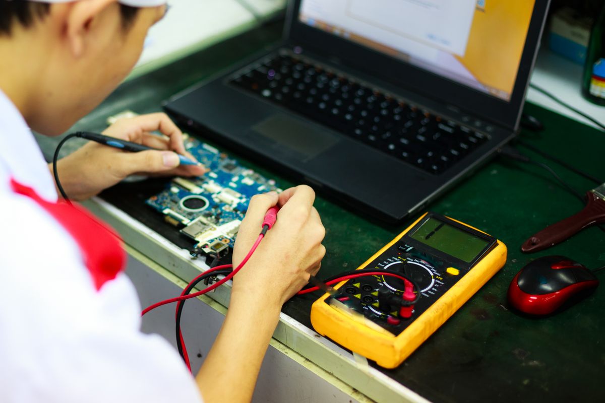 Técnico especialista reparando notebook con multímetro