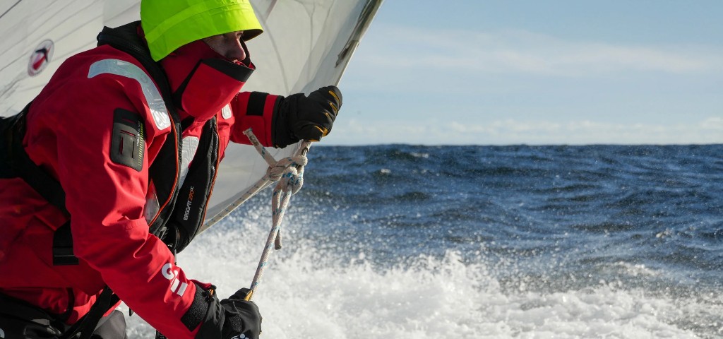 Tripulación navegando con ropa técnica roja y mar picado