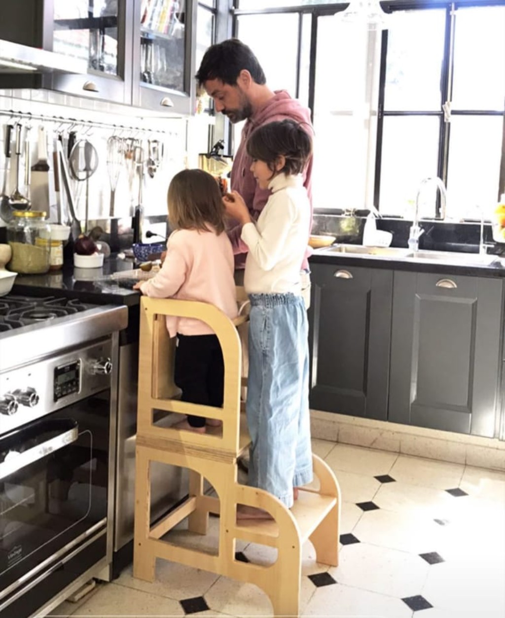 Un papá cocinando junto a sus dos hijos, de pie sobre la Torre de Aprendizaje Montedorf