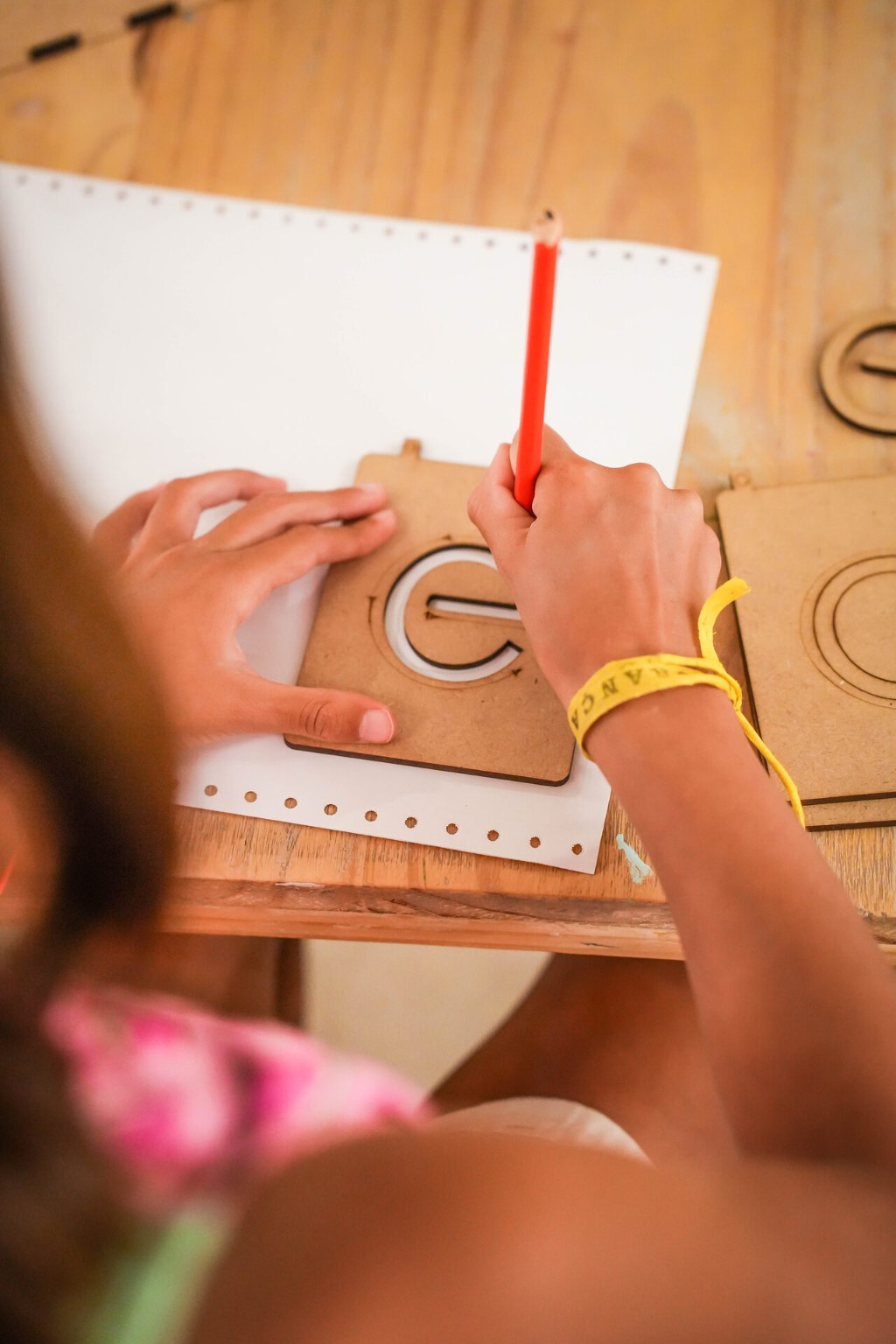 Manos de una ni&ntilde;a recorriendo con el dedo una letra de madera Montessori