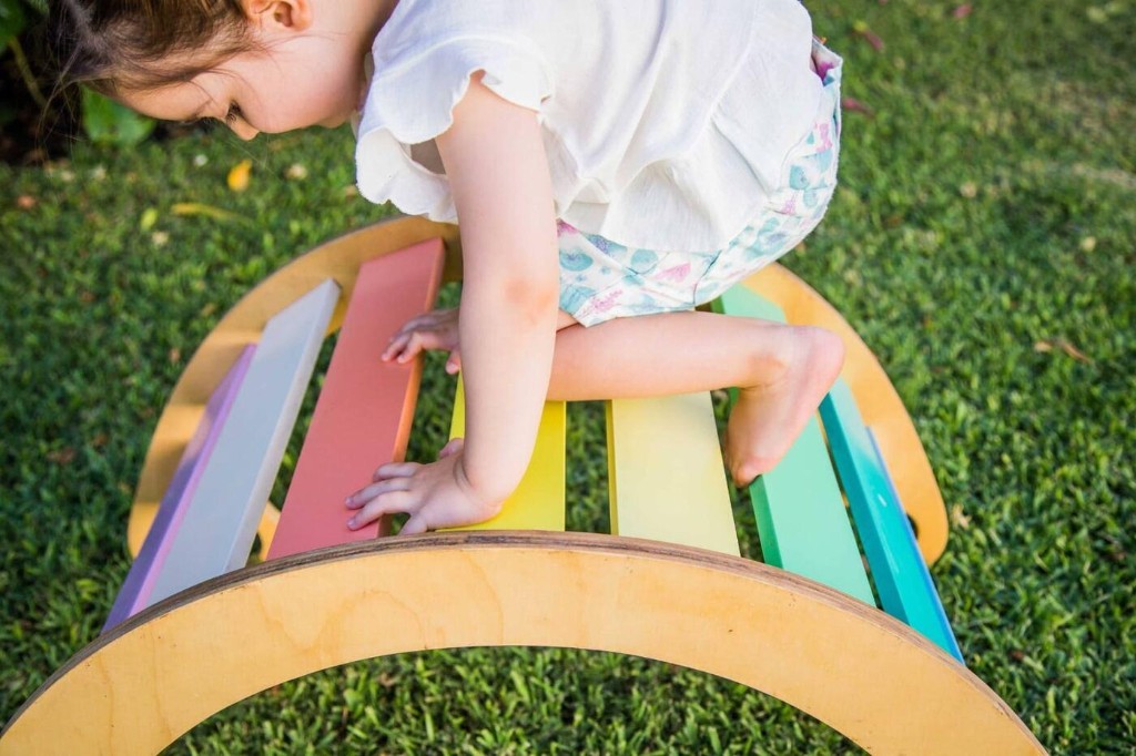 Ni&ntilde;a trepando el balanc&iacute;n Montessori de colores en el jard&iacute;n