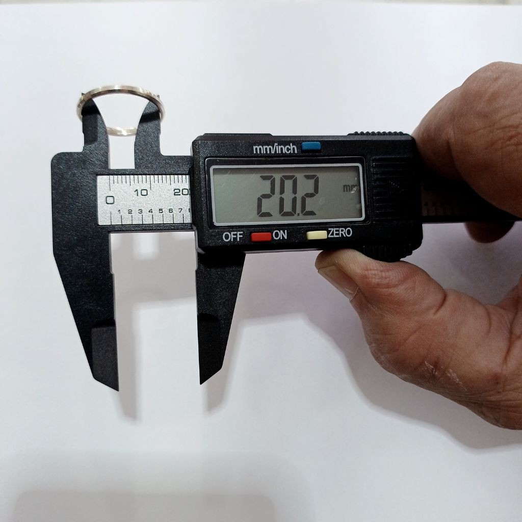 Medi&ccedil;&atilde;o profissional de joias: um paqu&iacute;metro digital mede o di&acirc;metro interno de uma alian&ccedil;a de prata, indicando o valor exato de 20.2 mm no visor para confer&ecirc;ncia de aro.