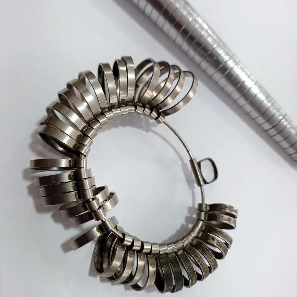 Ferramentas profissionais de joalheria: uma aneleira met&aacute;lica com diversos aros de tamanhos diferentes e um bast&atilde;o medidor de an&eacute;is (triboulet) sobre fundo branco