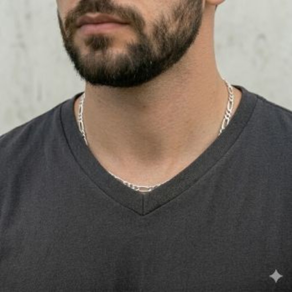 Close-up t&eacute;cnico padronizado do torso de um homem com barba, vestindo uma camiseta de gola V na cor carv&atilde;o escura. O fundo &eacute; um muro de concreto urbano claro. Ele usa uma corrente 3 em 1 (Figaro) maci&ccedil;a em Prata 925 polida, com 60cm de comprimento. A corrente est&aacute; completamente colocada por dentro da camiseta, sobre a pele, saindo apenas na parte central e acompanhando perfeitamente a linha do decote com caimento suave e texturizado.