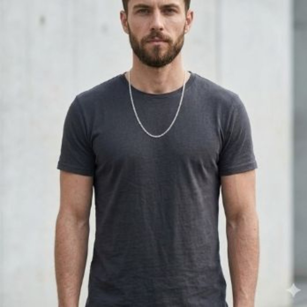 Estudo comparativo padronizado do torso de um homem esguio e porte magro, vestindo a mesma camiseta de gola careca na cor carv&atilde;o escura. O fundo &eacute; um muro de concreto urbano claro. Ele usa uma corrente Grumet maci&ccedil;a e achatada em Prata 925 polida, com 3mm de espessura e 60cm de comprimento. A joia tem escala refinada e caimento proporcional para o biotipo dele.