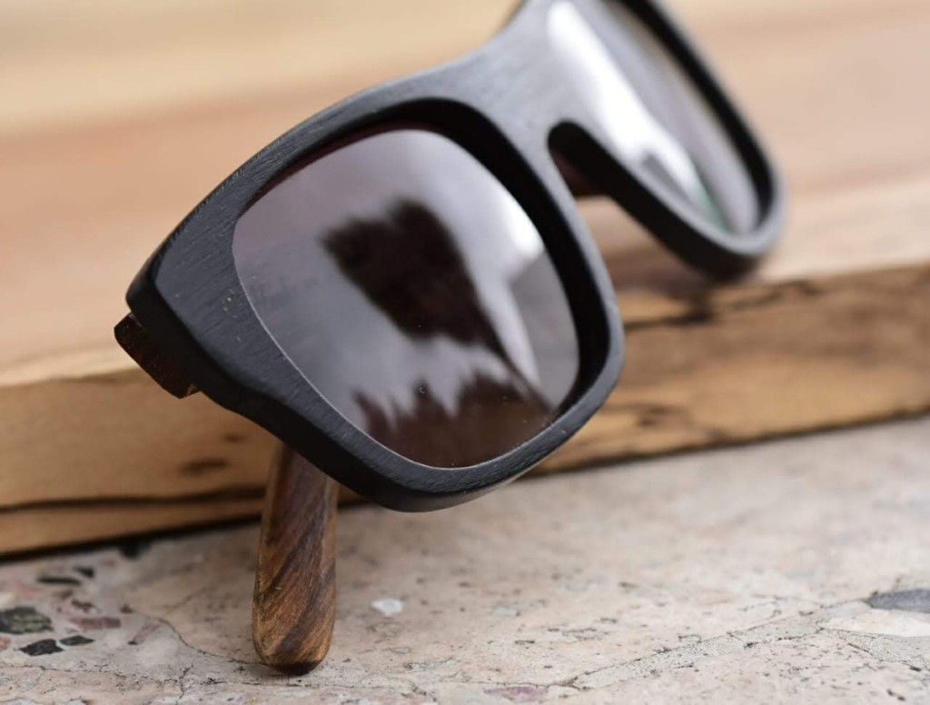 anteojos de sol de acetato negro mate y patillas de madera con forma rectangular modelo Berna marca Nomade sobre mesa de madera