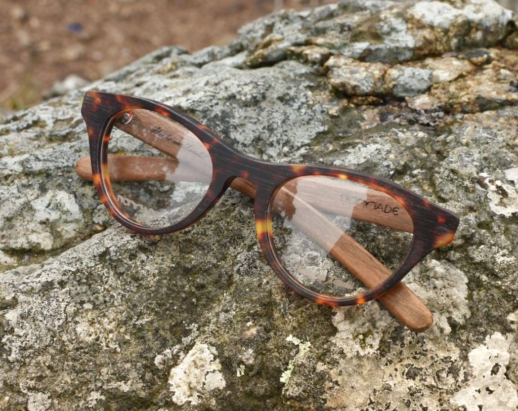 anteojos de estilo ojo de gato en acetato carey con patillas de madera marca Nomade sobre superficie de piedra en entorno natural
