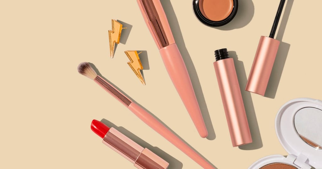 Colección de brochas de maquillaje y productos cosméticos dispuestos en composición flatlay sobre fondo rosa
