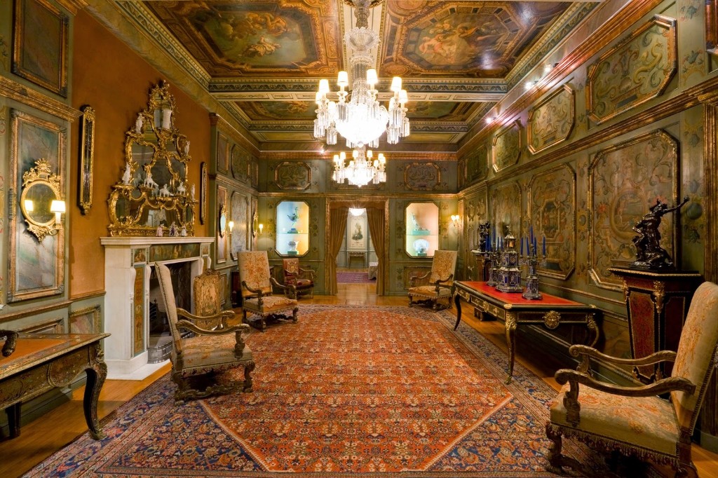 Interior de resid&ecirc;ncia hist&oacute;rica com decora&ccedil;&atilde;o barroca, marcado por **pain&eacute;is entalhados**, **talha dourada**, lustres de cristal e mobili&aacute;rio ornamentado. A integra&ccedil;&atilde;o entre arquitetura, arte e objetos revela como as casas aristocr&aacute;ticas eram concebidas como ambientes densamente decorados, onde cada detalhe refor&ccedil;ava prest&iacute;gio, cultura e sofistica&ccedil;&atilde;o est&eacute;tica.