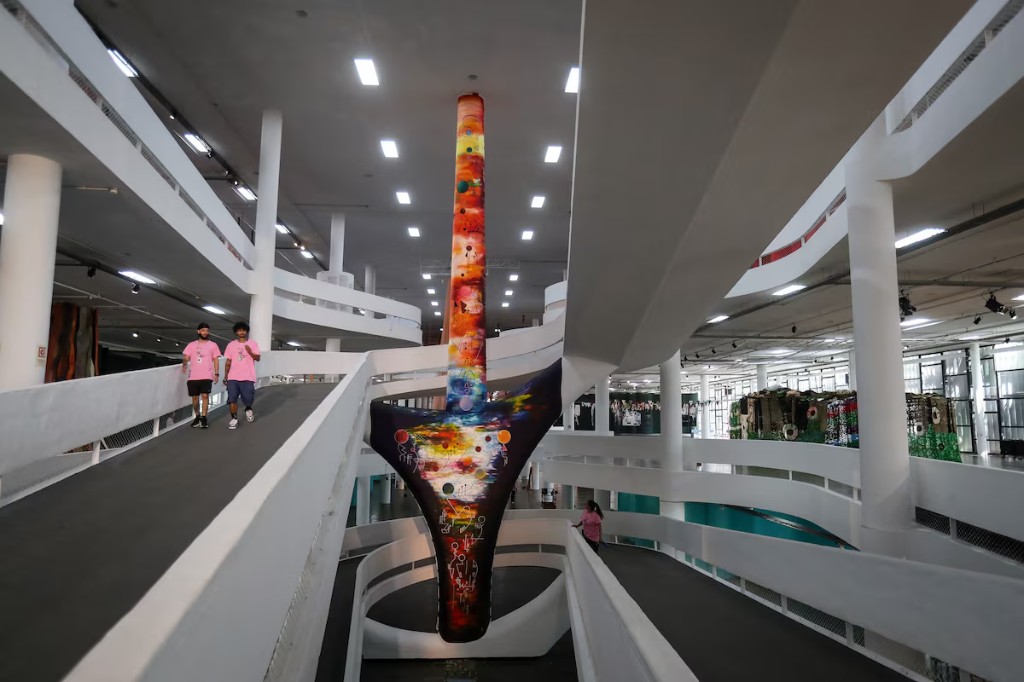 Interior do Pavilhão Ciccillo Matarazzo, no Parque Ibirapuera, em São Paulo, durante uma edição da Bienal de São Paulo. O espaço expositivo, projetado por Oscar Niemeyer, é conhecido por suas rampas contínuas e grandes áreas abertas que permitem a instalação de obras e projetos de arte contemporânea em grande escala.