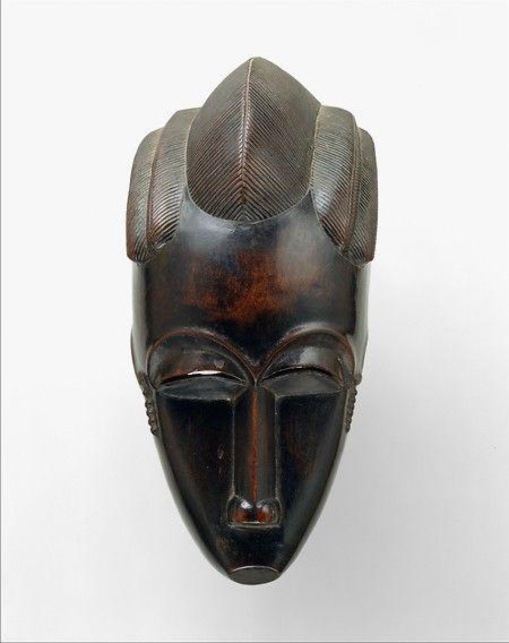 M&aacute;scara africana do povo Fang, origin&aacute;rio do Gab&atilde;o e de regi&otilde;es da &Aacute;frica Central, marcada pelas fei&ccedil;&otilde;es alongadas, superf&iacute;cies suavizadas e forte presen&ccedil;a simb&oacute;lica associada ao culto dos ancestrais. Obras como esta exerceram grande influ&ecirc;ncia sobre artistas modernistas europeus do in&iacute;cio do s&eacute;culo XX, especialmente no desenvolvimento do Cubismo e da est&eacute;tica moderna.