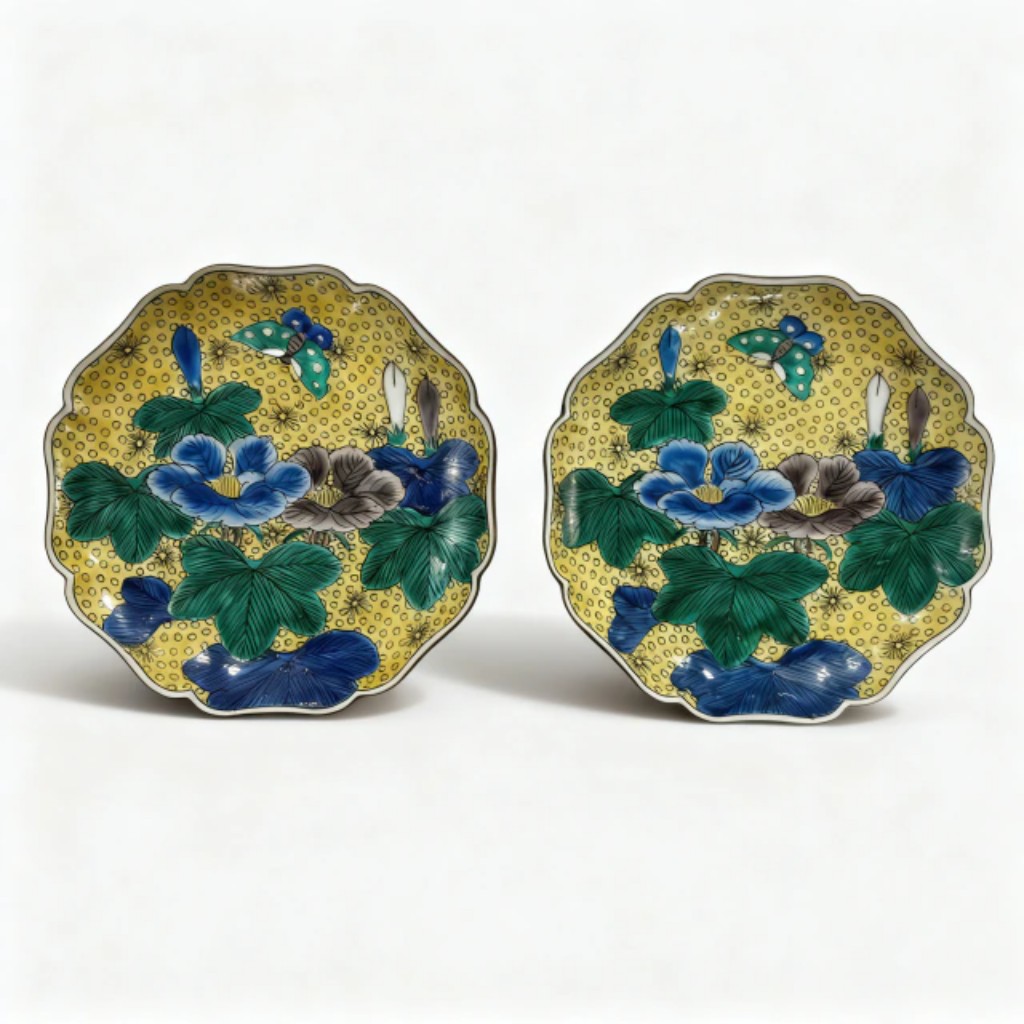 Par de covilhetes polilobados em porcelana japonesa Kutani, com decora&ccedil;&atilde;o na paleta Aote / Yoshidaya (amarelo, verde, azul e violeta), apresentando pe&ocirc;nias, folhagens e borboleta sobre fundo amarelo pontilhado. Verso esmaltado em verde com folhagens, marcado ao centro com assinatura em cartela esmaltada. Obra japonesa do s&eacute;culo XIX, da renomada porcelana Kutani.
