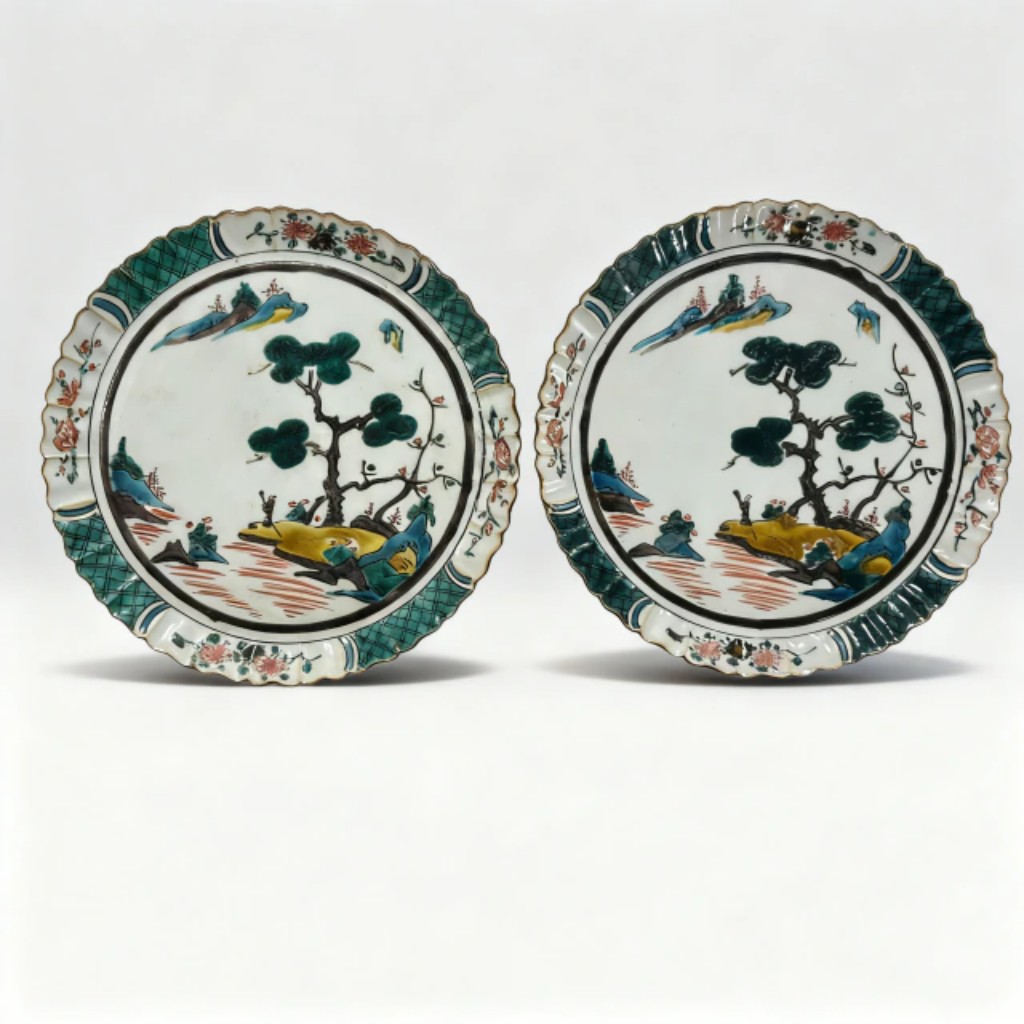 par de pratos em porcelana Kutani, Jap&atilde;o, s&eacute;culo XVIII, decorados em esmalta&ccedil;&atilde;o policromada com paisagem oriental estilizada, aves e elementos naturais, apresentando a tradicional paleta em verde, azul, amarelo e ferro vermelho caracter&iacute;stica das primeiras produ&ccedil;&otilde;es Kutani. Pe&ccedil;as de forte influ&ecirc;ncia est&eacute;tica do per&iacute;odo Edo, marcadas pelo refinamento pict&oacute;rico e composi&ccedil;&atilde;o ornamental exuberante. 