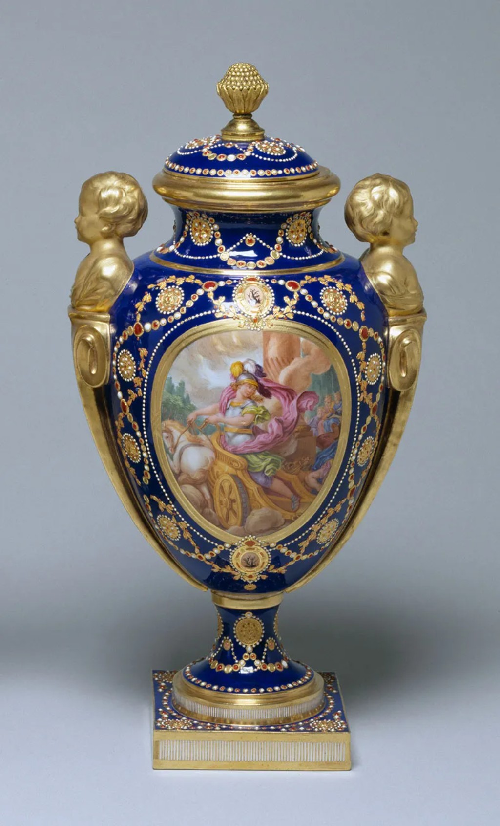Grande vaso ornamental em porcelana de S&egrave;vres com decora&ccedil;&atilde;o em azul profundo e doura&ccedil;&atilde;o exuberante, representando o luxo e a sofistica&ccedil;&atilde;o art&iacute;stica da manufatura francesa que se tornou s&iacute;mbolo das artes decorativas europeias a partir do s&eacute;culo XVIII. Pe&ccedil;as como esta eram produzidas para a corte francesa e utilizadas como demonstra&ccedil;&atilde;o de prest&iacute;gio, poder e refinamento cultural.