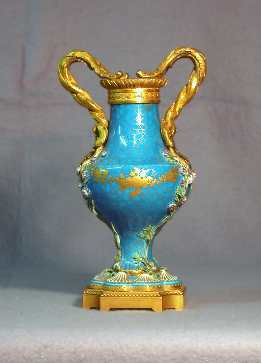 Vaso monumental produzido pela Manufatura de S&egrave;vres durante o per&iacute;odo do Imp&eacute;rio Napole&ocirc;nico, quando a porcelana francesa tornou-se uma importante ferramenta de representa&ccedil;&atilde;o pol&iacute;tica e diplom&aacute;tica. Inspiradas na est&eacute;tica da Roma Antiga, as pe&ccedil;as desse per&iacute;odo destacavam-se pelas formas grandiosas, pela rica aplica&ccedil;&atilde;o de doura&ccedil;&atilde;o e pela presen&ccedil;a de s&iacute;mbolos imperiais que exaltavam o poder de Napole&atilde;o Bonaparte. Obras como esta eram frequentemente encomendadas para decorar pal&aacute;cios, presentear membros da elite europeia e refor&ccedil;ar a imagem da Fran&ccedil;a como principal pot&ecirc;ncia art&iacute;stica e cultural do continente. A combina&ccedil;&atilde;o entre excel&ecirc;ncia t&eacute;cnica, sofistica&ccedil;&atilde;o decorativa e significado pol&iacute;tico faz das porcelanas imperiais de S&egrave;vres alguns dos exemplares mais admirados e valorizados da hist&oacute;ria das artes decorativas europeias.