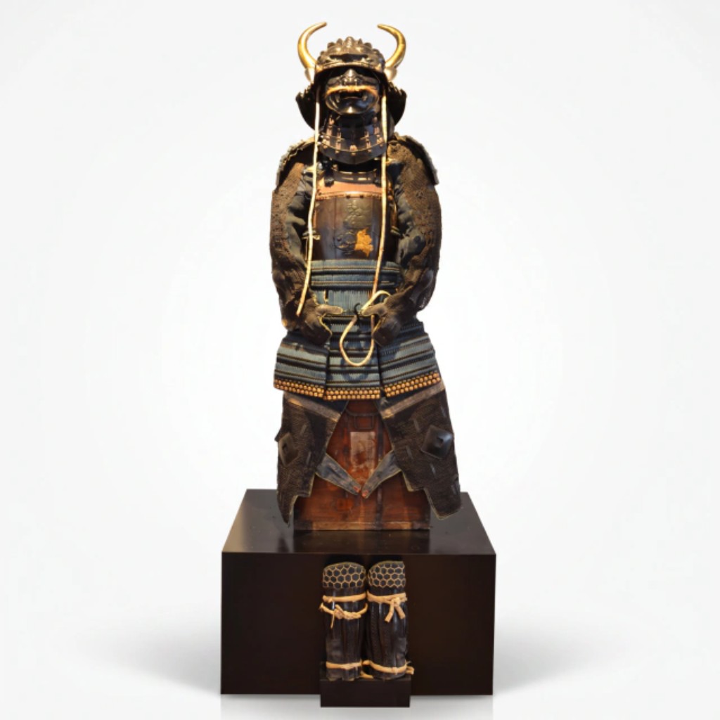 Impressionante armadura de samurai (yoroi/gusoku) do período Edo (1603-1868), composta por kabuto (elmo) rematado por kuwagata (chifres frontais dourados), menpō (máscara facial em laca preta com bigode), dō (couraça peitoral) em laca com shishi (leão guardião) e peônia (botan) em relevo dourado, sode (protetores de ombro), kote (mangas de malha de ferro), kusazuri (saiote de placas), haidate (protetores de coxa) e suneate (caneleiras). Acompanha caixa original em madeira com etiqueta caligráfica em kanji provavelmente indicando proveniência da antiga província de Mino (atual prefeitura de Gifu). Japão, cerca de 1800.