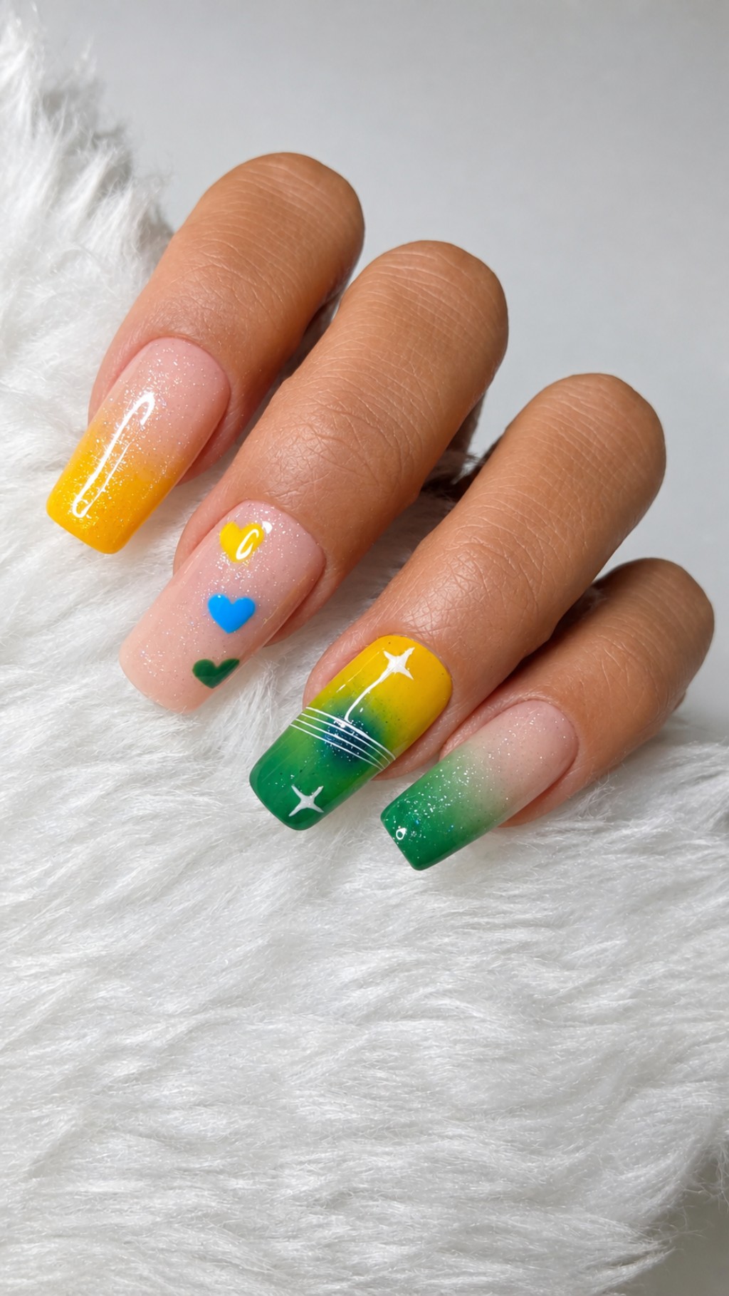 Close de unhas posti&ccedil;as decoradas inspiradas na Copa do Mundo com degrad&ecirc; verde e amarelo, glitter suave e nail art moderna em acabamento brilhante.