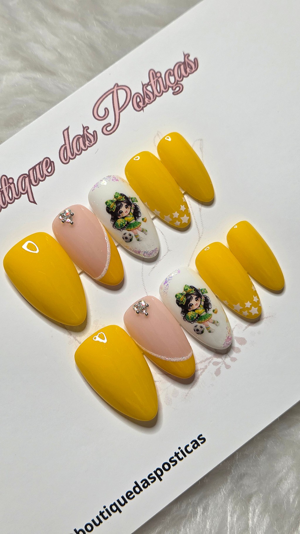 Kit de unhas posti&ccedil;as decoradas em amarelo, branco e nude com pedraria, estrelas e personagem delicada inspirada na torcida brasileira.