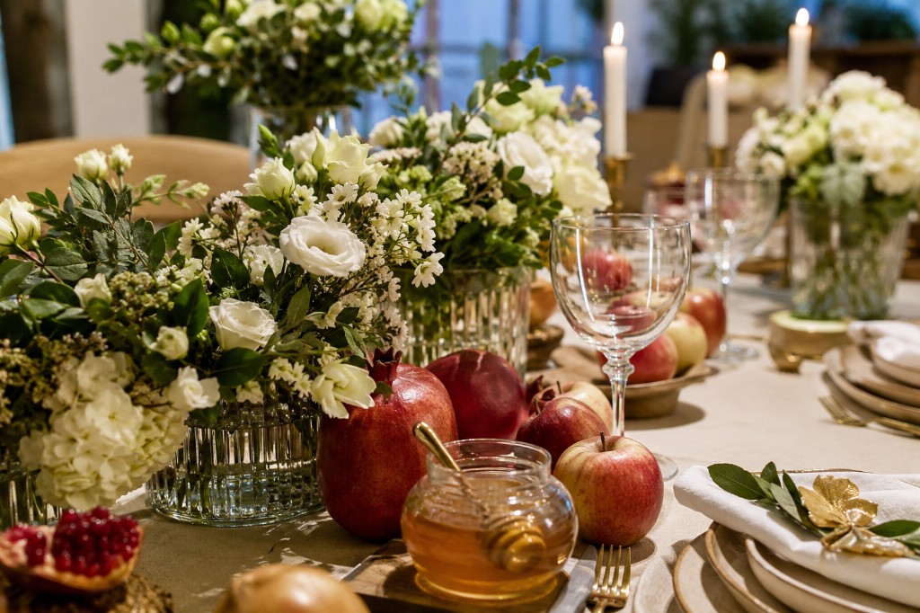Decoración de mesa para Rosh Hashaná con flores blancas, granadas y detalles en tonos miel