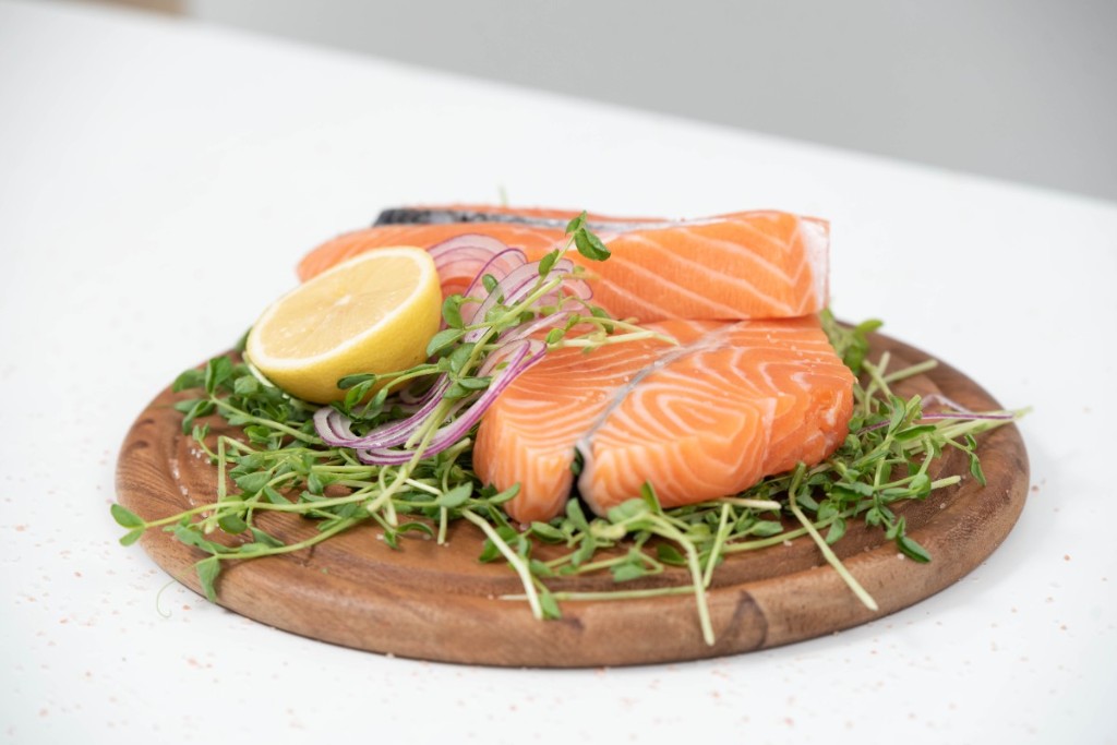 Peda&ccedil;os de salm&atilde;o cru cortados em um prato com lim&atilde;o e ramos verdes.