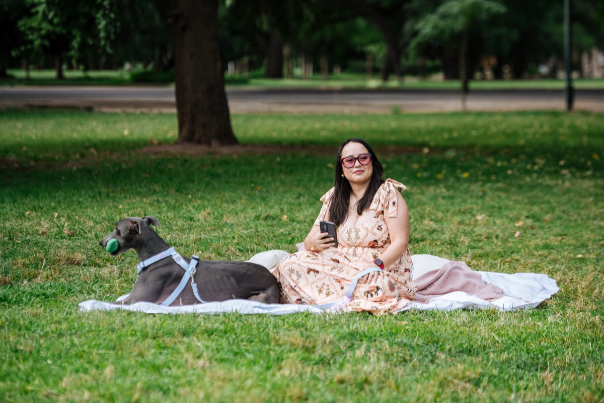 Chica descansando a la sombra en un parque con su perro chico en brazos