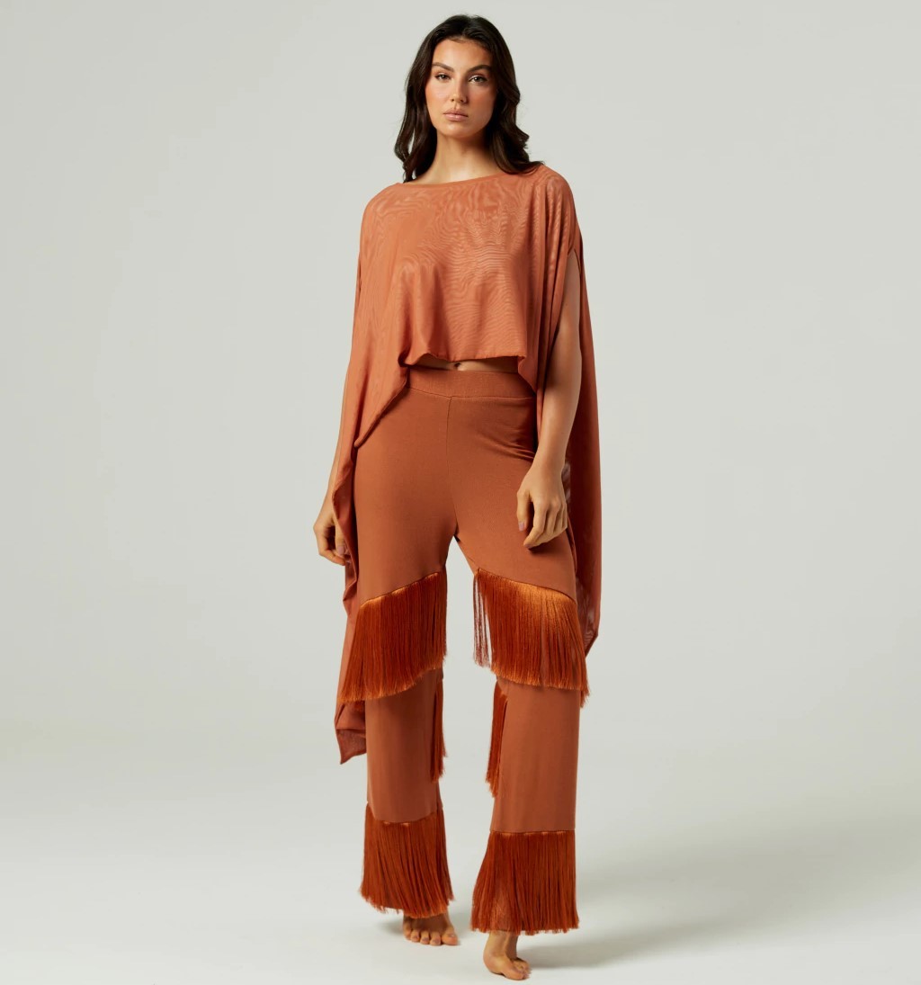 Mulher vestindo um look country com blusa leve e cal&ccedil;a de franja, ambos em tom marrom terroso.