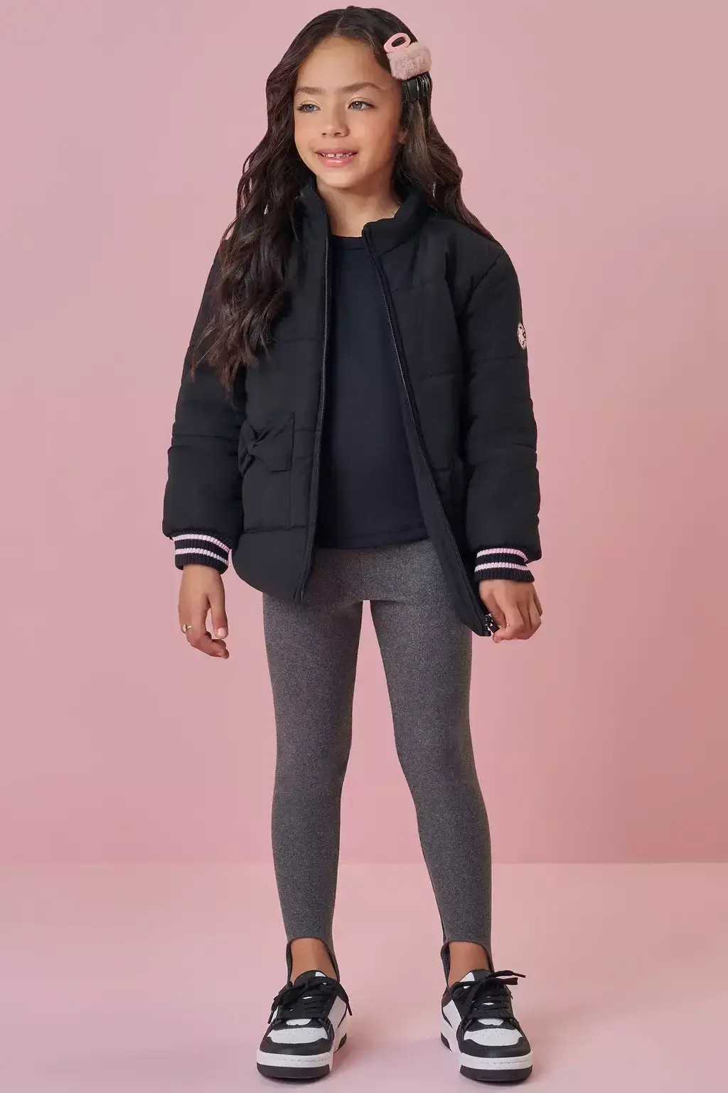 Menina usando legging infantil com pezinho, jaqueta preta, blusa b&aacute;sica e t&ecirc;nis, em look confort&aacute;vel para passeios nos dias mais frios.