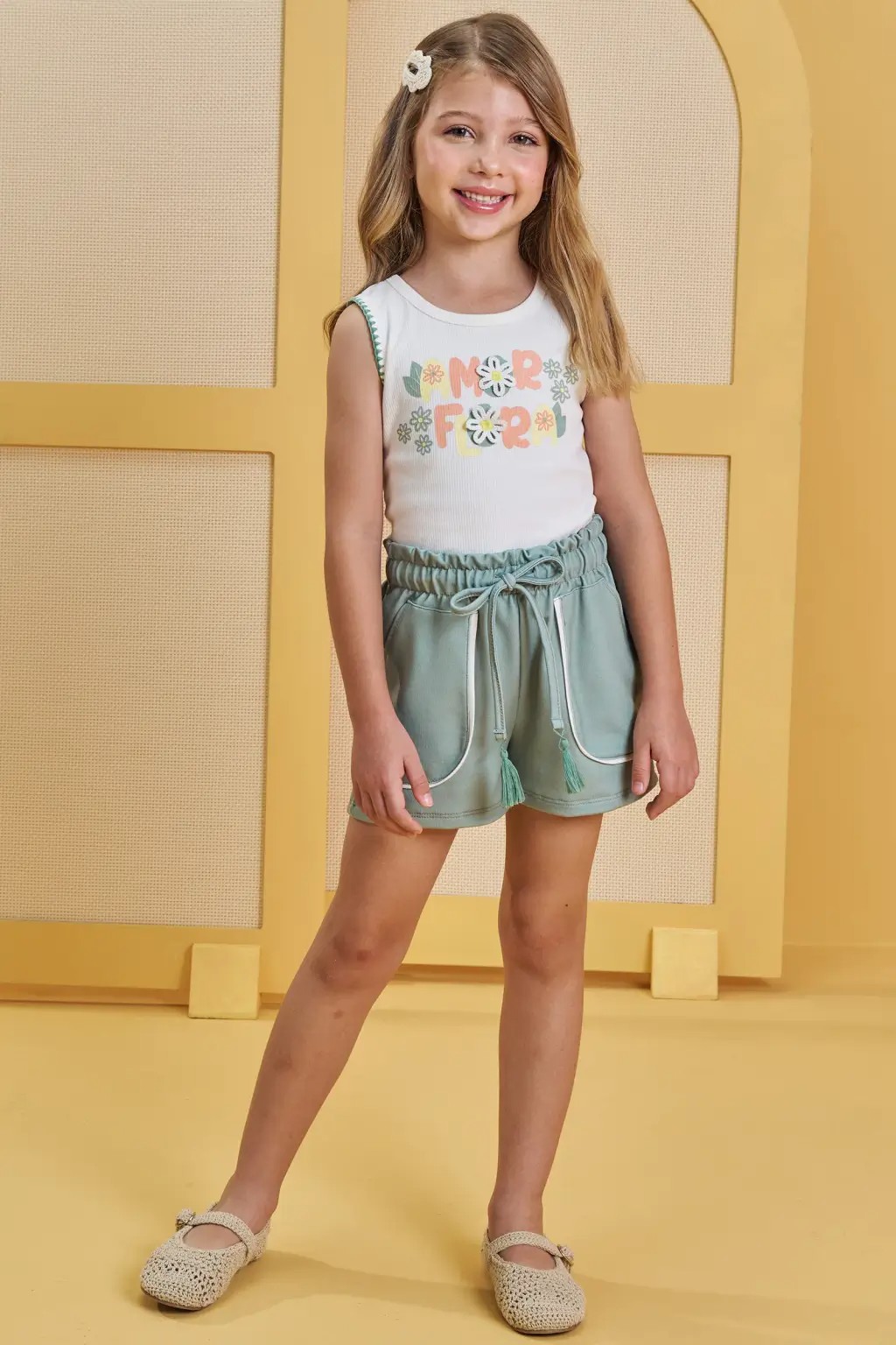 Menina usando conjunto infantil com blusa regata, short verde e sapatilha, ideal para passeios e atividades nas f&eacute;rias escolares.