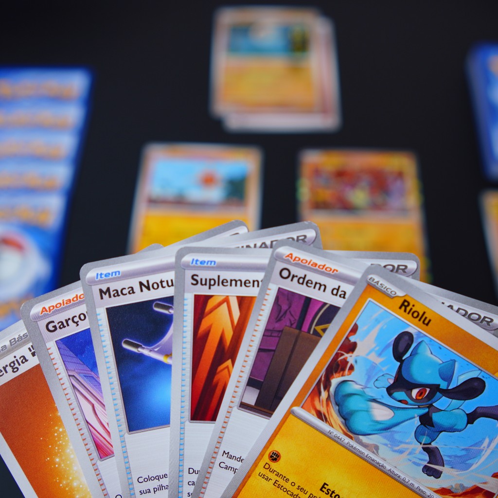 Mesa de jogo montada e jogador segurando cartas de Pokémon TCG em partida