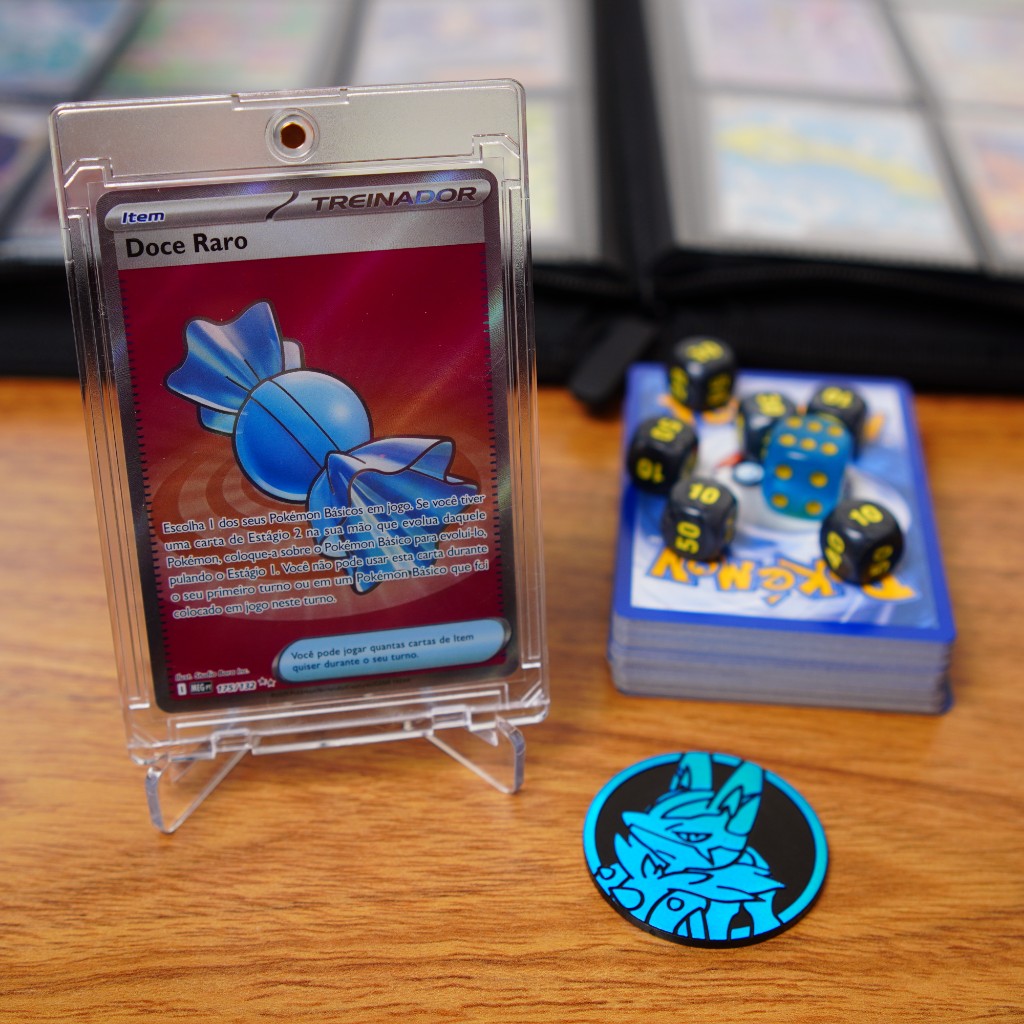 Carta protegida e baralho com acess&oacute;rios ao lado com binder de cole&ccedil;&atilde;o ao fundo