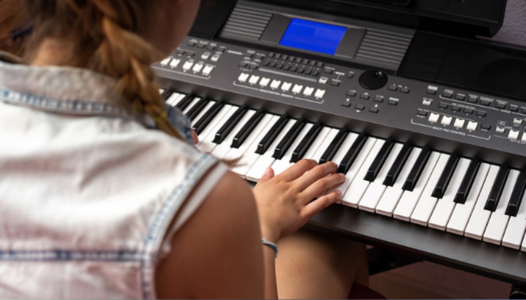 Crian&ccedil;a tocando teclado eletr&ocirc;nico durante atividade de aprendizado musical