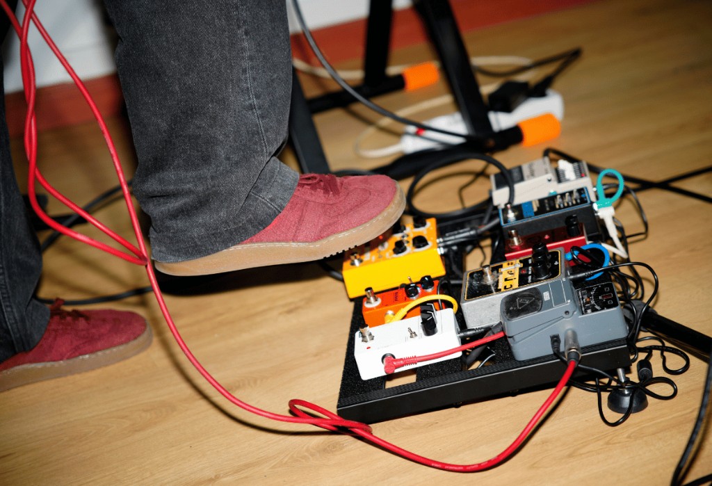 Pedais de guitarra encaixados em um pedalboard, ligados por cabos curtos, durante ensaio