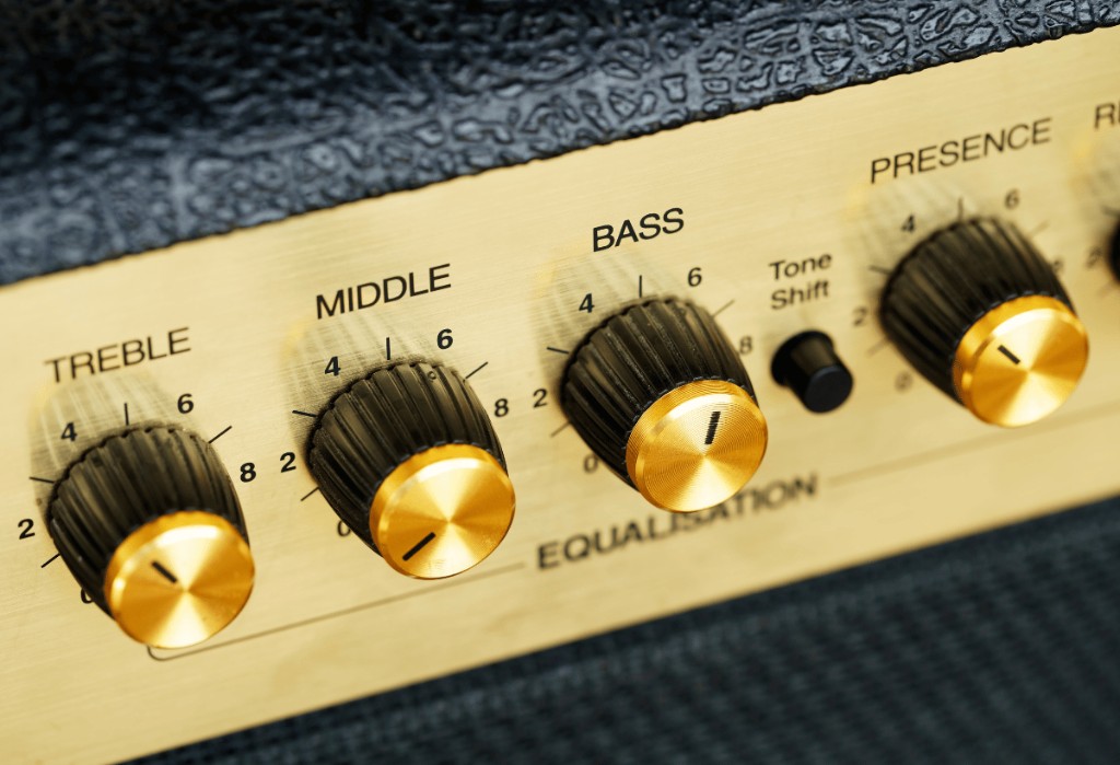 Painel dourado de amplificador de guitarra em close, com os knobs de equalização Treble, Middle, Bass e Presence