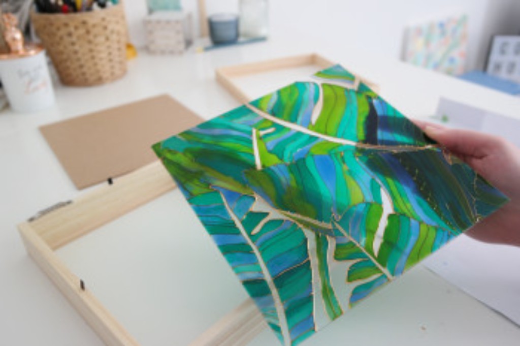 Painel decorativo de folhas verdes e azuis com contornos dourados.